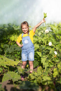 Little smiling girl holding a branch in her hands with white pumpkins and leaves in the garden.