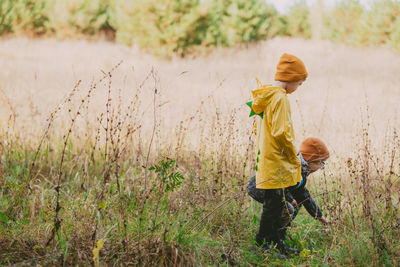 Boys are walking in the autumn field. a boy in a yellow raincoat walks 