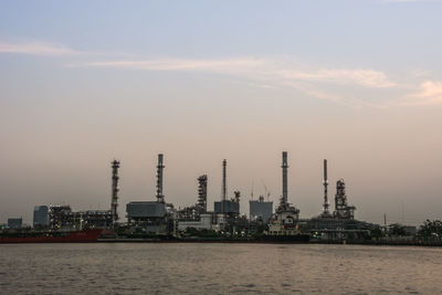 View of oil refinery by sea during sunset against sky