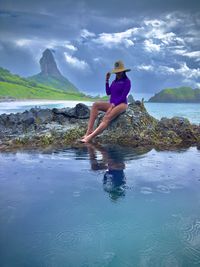 Full length of young woman standing in sea against sky