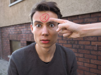 Cropped image of hand pointing at man face with sad emoticon