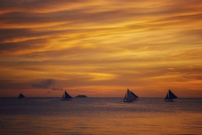 Sailboats sailing on sea against orange sky