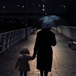 Rear view of women with daughter walking on footpath at night