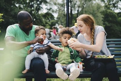 Parents feeding children while sitting on bench at park