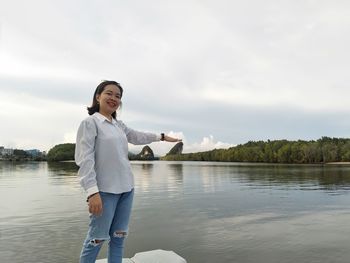 Young woman standing by lake against sky