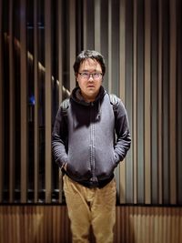 Portrait of young asian man in eyeglasses standing against patterned wall.