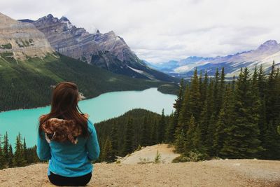 Rear view of young woman looking at view while standing on mountain against cloudy sky