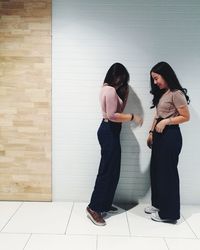 Full length of friends standing on tiled floor by wall