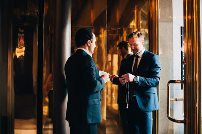 Smiling mature businessman talking while standing against glass at coffee shop