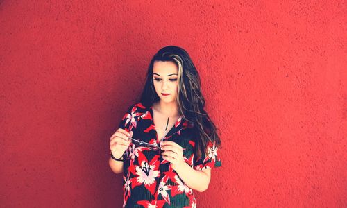 Young woman standing against red wall