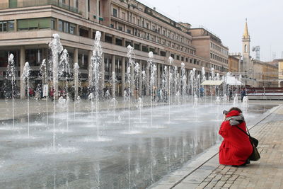 Rear view of woman with fountain against buildings in city