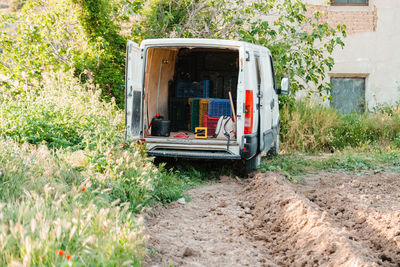 Van parked in a crop field with open doors an crates and agricultural tools inside