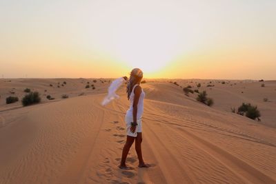 Woman standing on sand dune in desert against sky