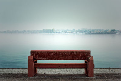 Empty bench by lake against clear sky
