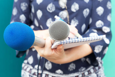 Midsection of female journalist holding notepad and microphones against colored background