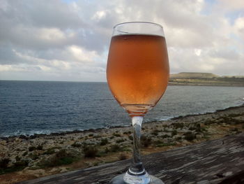 Close-up of beer glass against sea during sunset