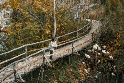 High angle view of young adult woman standing on wooden path in forest in autumn.