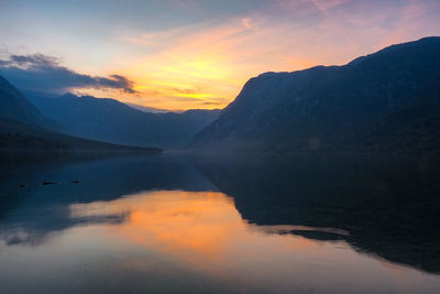 Scenic view of lake by mountains against sky during sunset