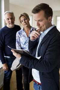 Male real estate agent reading agreement with couple standing in background at home