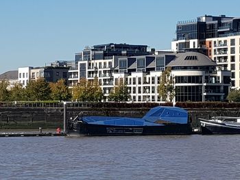 Buildings by river against clear blue sky