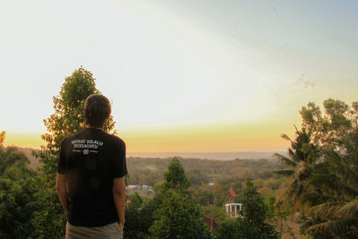 Rear view of man standing by plants against sky