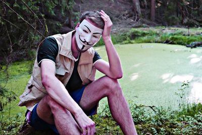 Portrait of man wearing mask sitting by pond