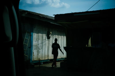 Rear view of silhouette man standing by building against sky