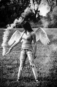 Woman with angle wing holding distress flare on field