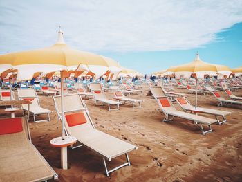 Lounge chairs and parasols on beach against sky