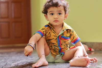 A child sitting on the ground inside the house and a little boy with one hand on his knee