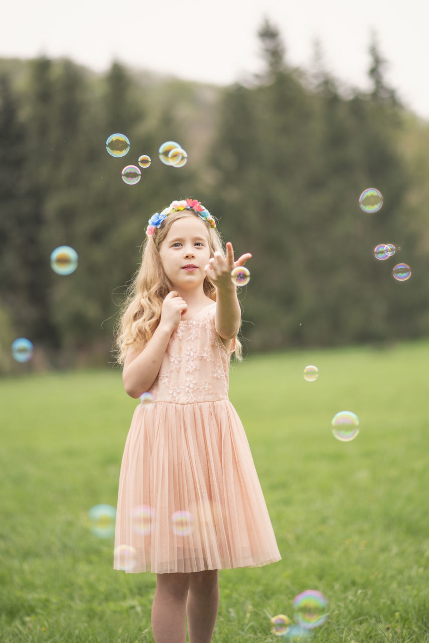 bubble, one person, women, leisure activity, mid-air, girls, plant, nature, focus on foreground, grass, real people, three quarter length, bubble wand, standing, females, child, field, land, hair, outdoors, innocence, hairstyle