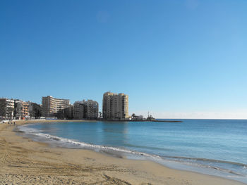 Sea by buildings against clear blue sky