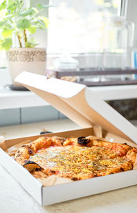 Cheese pizza in an ajar box on a white table by the window. order food home