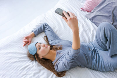 Beautiful woman in blue pajamas looking into phone. morning starts with phone.