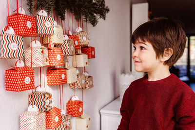 Little child waiting to start opening handmade advent calendar hanging on wall. 