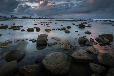 Rocks on beach against sky during sunset