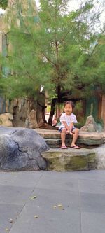 Full length of boy sitting on stone wall