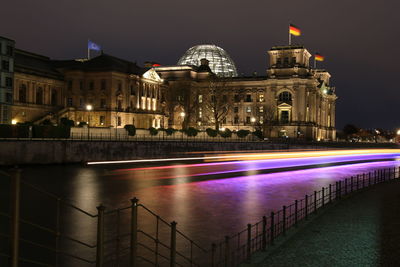 Light trails on canal by buildings at night