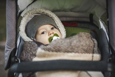 Portrait of cute toddler with pacifier in mouth lying on baby stroller at park during autumn