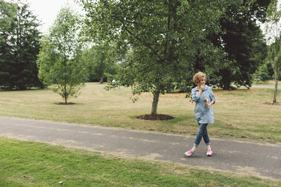 Full length of young woman eating while standing on walkway at park