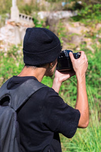 Young photographer in a wool hat makes a photo on his camera - young man with backpack 