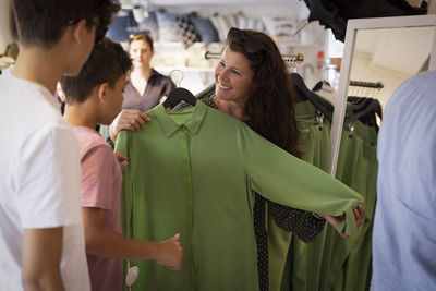 Happy woman showing green dress to sons standing in store