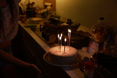 Midsection of woman holding illuminated candle on the birthday cake