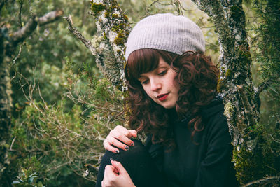 Young woman sitting by tree in forest