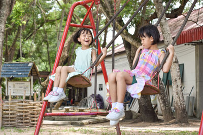 Two asian little sisters having fun on swing together in park on sunny day outdoor. selective focus