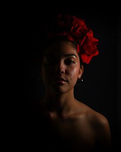 Portrait of young woman wearing flowers against black background