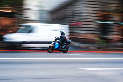 Rear view of man riding motor scooter on street