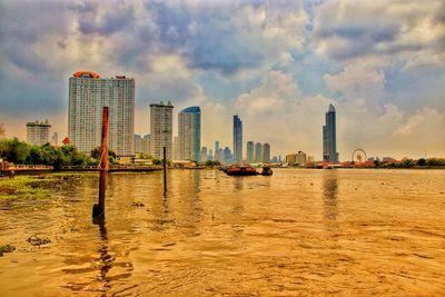 City buildings by river against sky