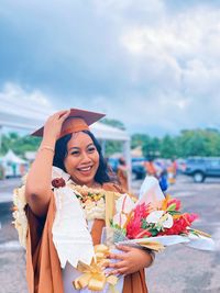 Portrait of woman wearing graduation gown standing against sky