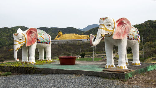 Elephant standing by statue against sky